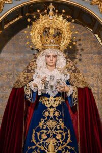 la venerada imagen luce saya de terciopelo azul bordada en oro, manto rojo en terciopelo liso y toca de sobremanto bordada en oro sobre malla